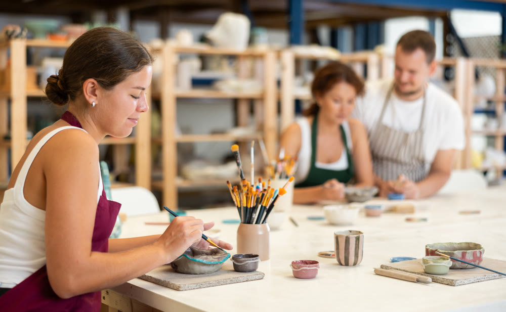 Girl in apron designing handmade clay plate with brush in taller room