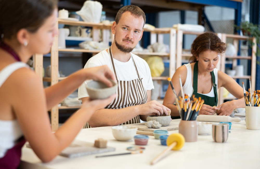 Three pottery workshop workers sculpt from raw clay