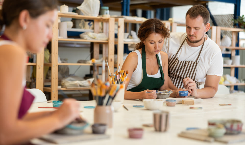 Male pottery teacher helps students shape clay into plates and dishes