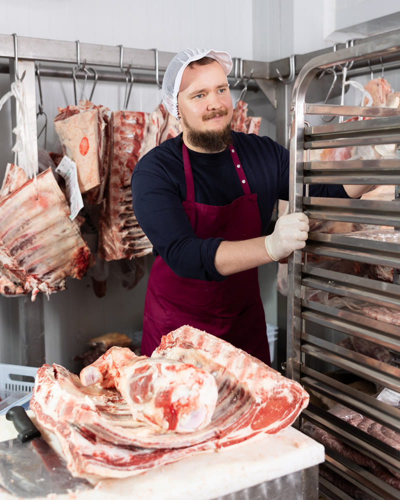Portrait of male butcher while working in a butcher shop - moving trays with chopped carcasses