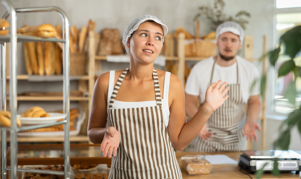 In bakery, confused female employee during quarrel with guy boss