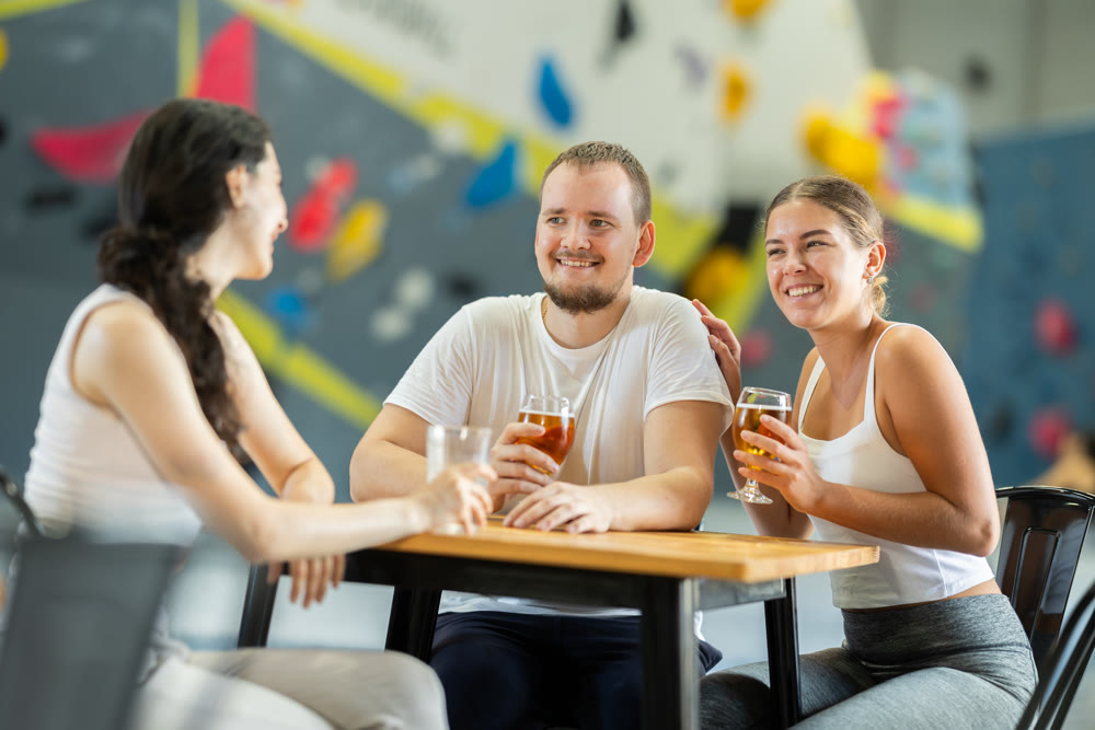 Man and two women talk at table on climbing wall