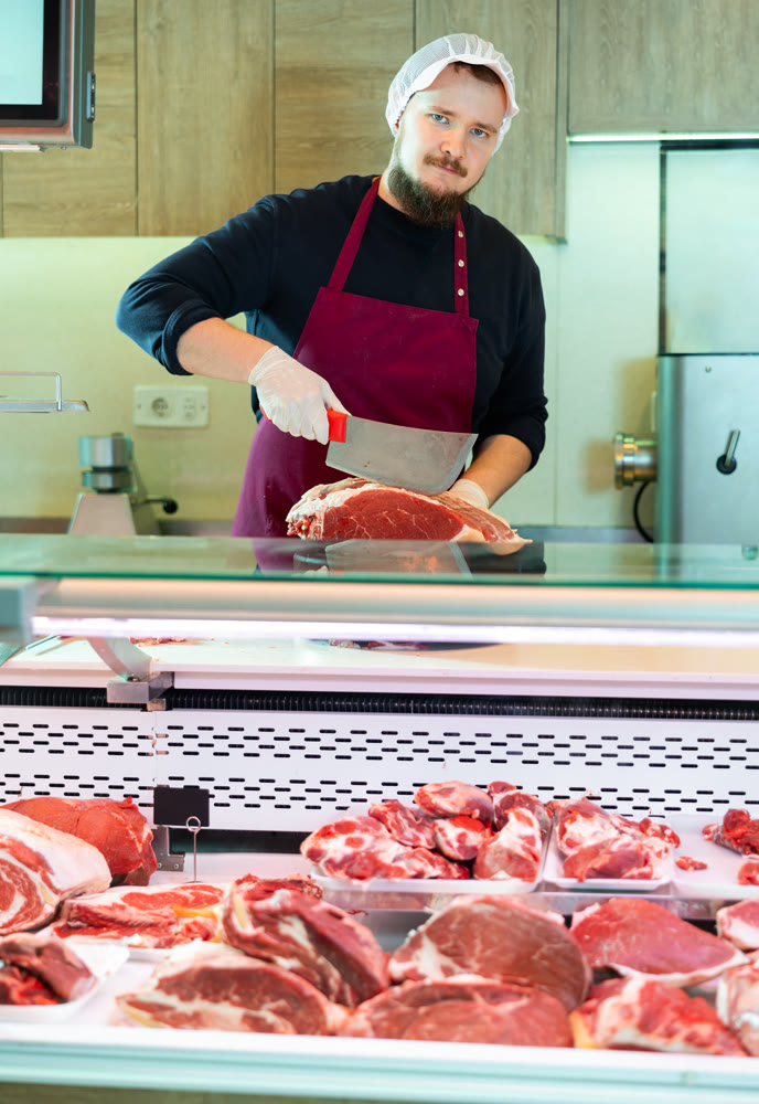 Butcher cuts piece of raw meat for sale in the meat department of supermarket