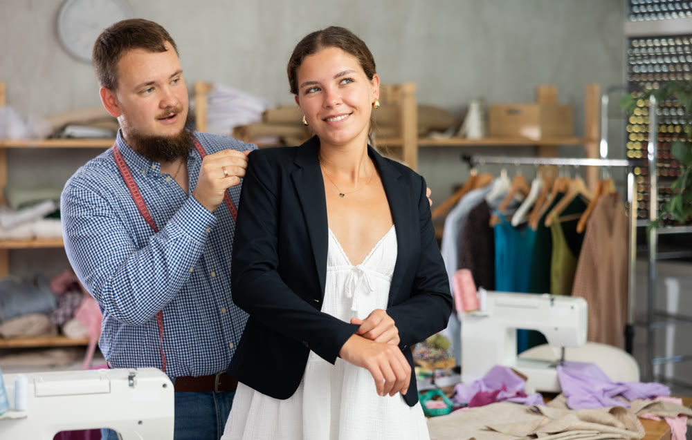 Tailor adjusting jacket on female client in sewing studio
