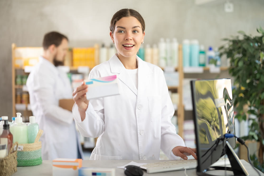 Pharmacist works in a pharmacy against the background of an male assistant who puts goods on the shelves