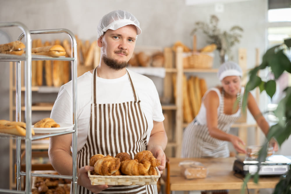 Male seller holds basket with finished products, shows many croissants