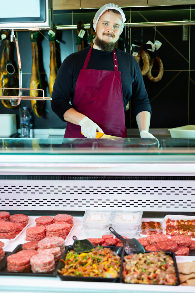 Man butcher holding meat cutlets in meat section of supermarket