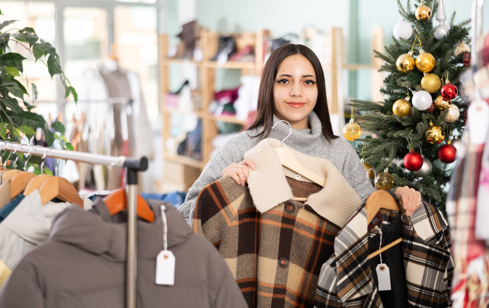 Female shopper chooses coat or jacket in clothing store before Christmas