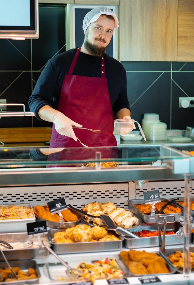 Male butcher placing tray of meat stew on shop window
