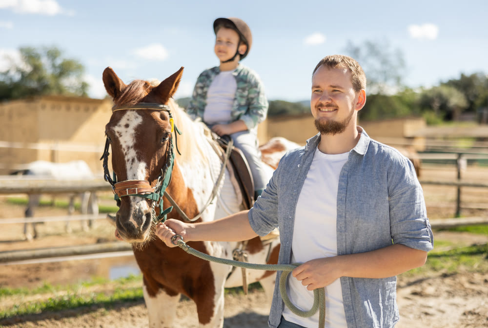 Young man leads horse with boy riding