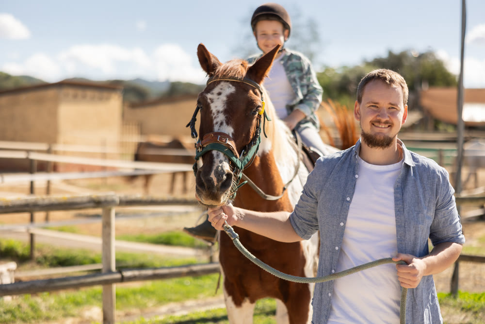 Young man leads horse with boy riding