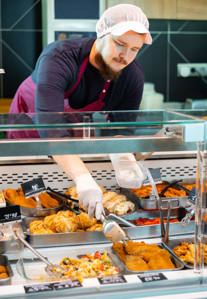 Male butcher placing tray of meat stew on shop window