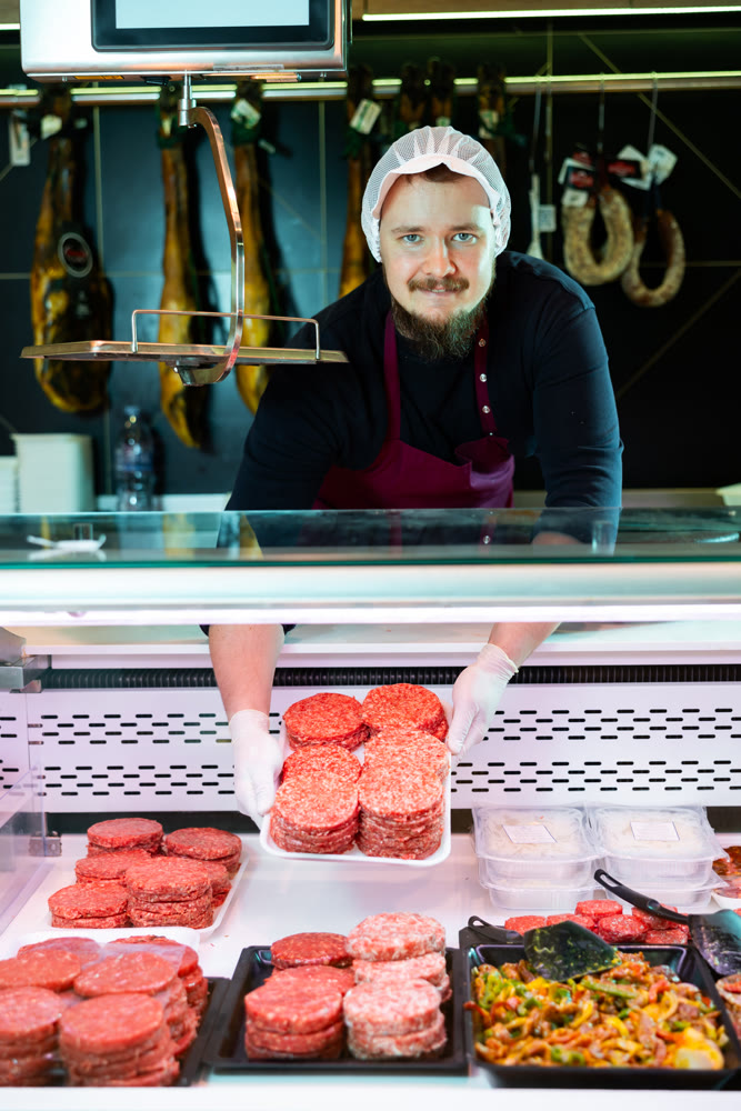 Man butcher holding meat cutlets in meat section of supermarket