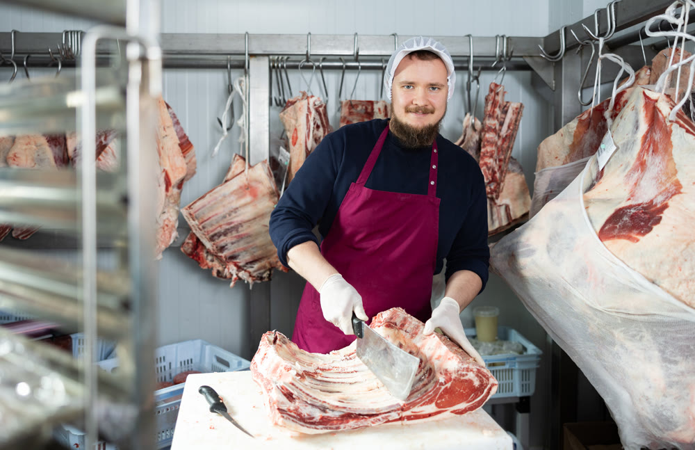 Employee of local butcher shop divides large huge piece of meat carcass with knife