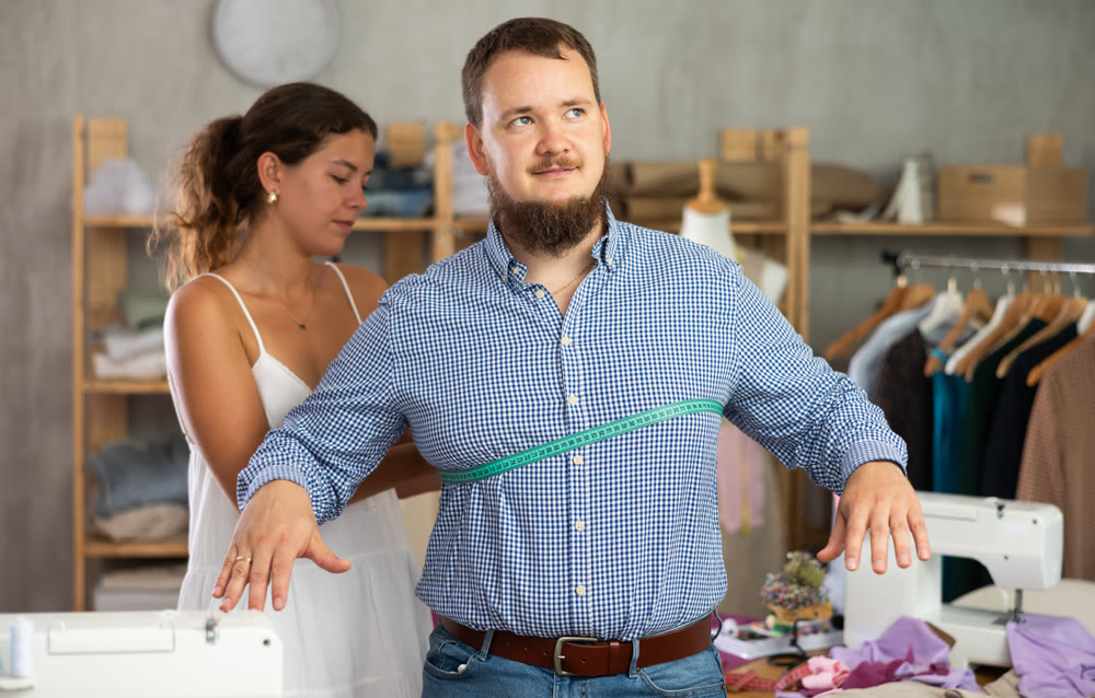 Young female dressmaker measuring male client