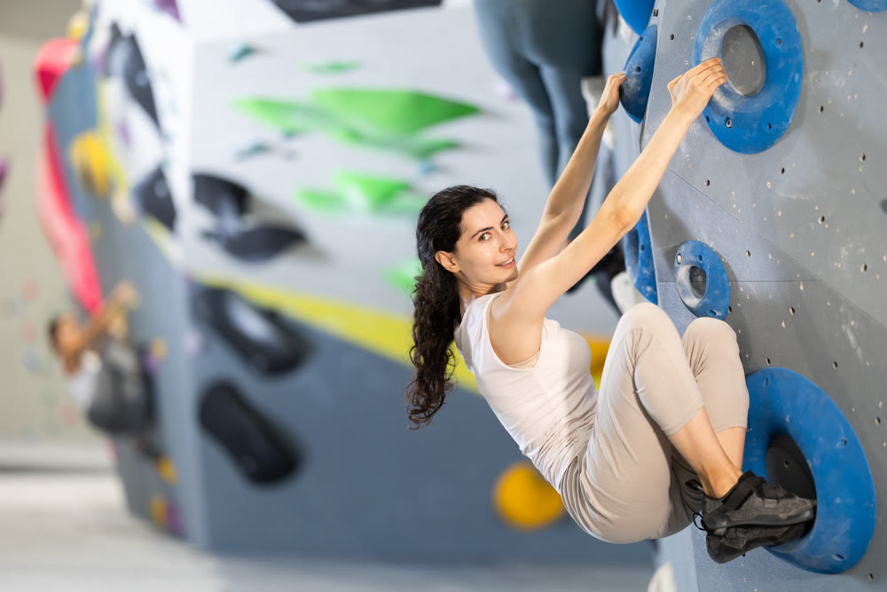 Motivated young girl climbing without ropes and harnesses on artificial bouldering wall in fitness center