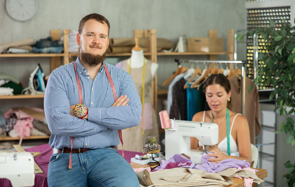 Bearded tailor sitting on table in sewing studio