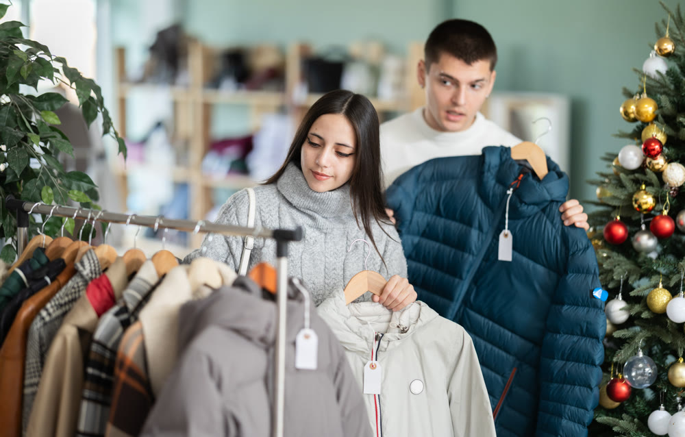 Portrait of happy married couple choose coat or jacket for girl against background of Christmas tree in store