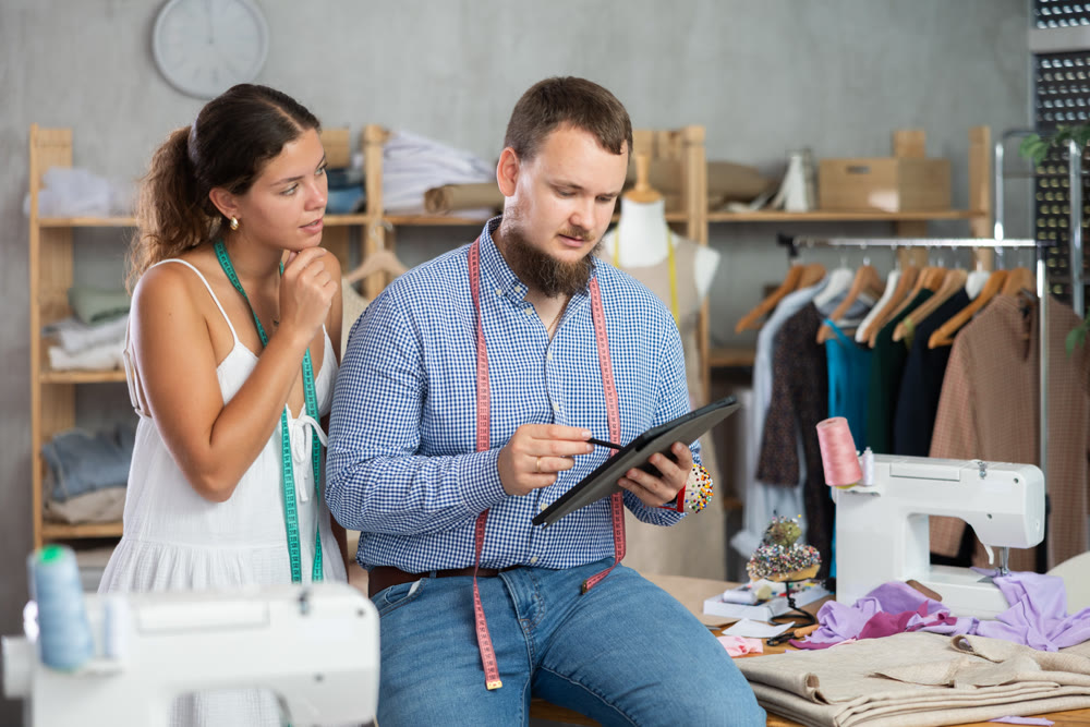 Male dressmaker discussing with girl the sketch on tablet