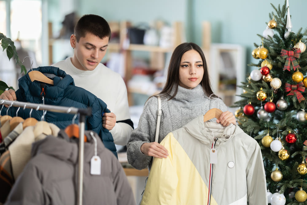 Portrait of happy married couple choose coat or jacket for girl against background of Christmas tree in store