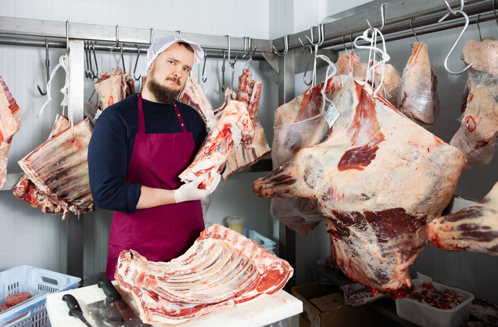 Bearded butcher shop seller preparing beef cuts for sale