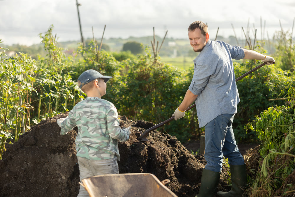 Young man and boy putting soil in wheelbarrow