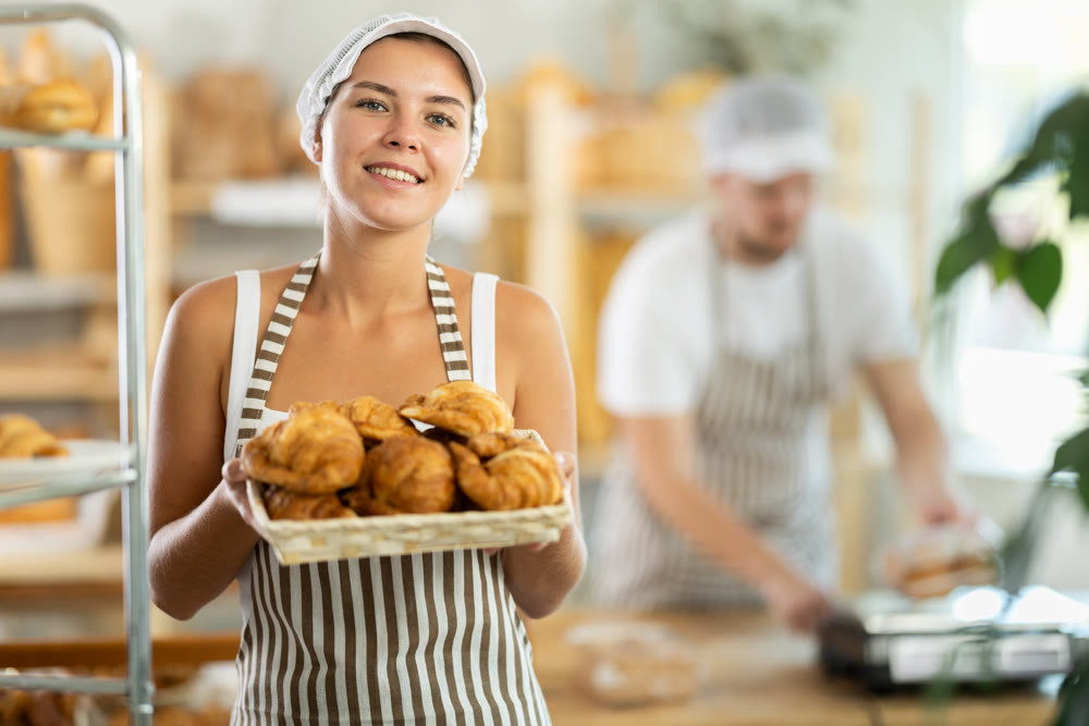 Young saleswoman displays croissants in square wicker basket