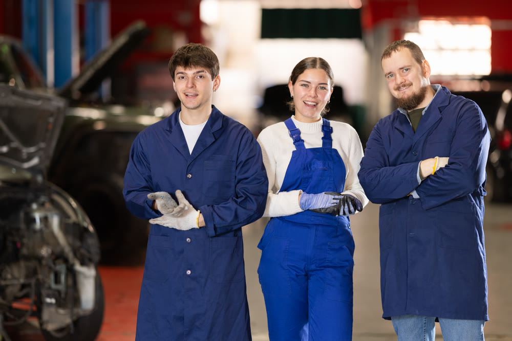 Team of auto mechanics, two men and one woman, wearing blue overalls and posing, ready to provide professional vehicle service