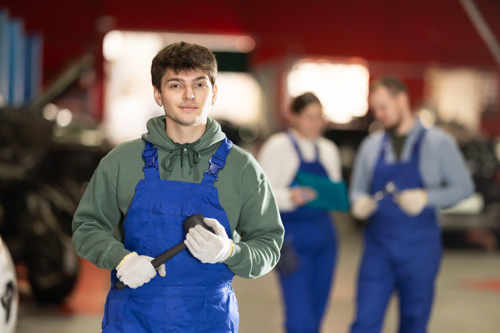 Auto mechanic in uniform standing by automobile in car workshop