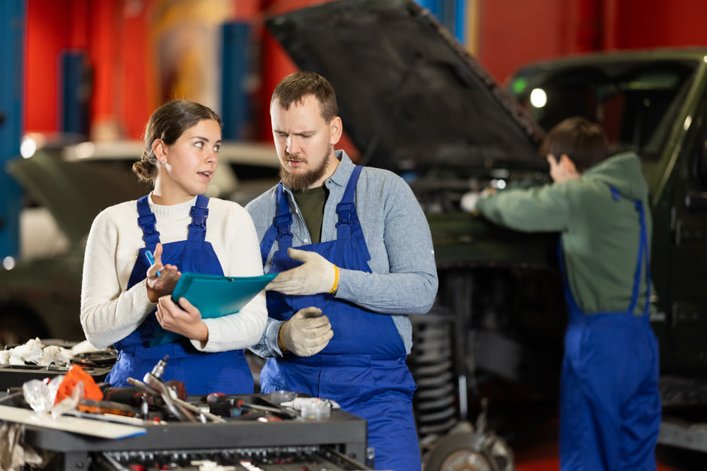 Car service manager discusses car repair problems with mechanic. He takes notes on paper