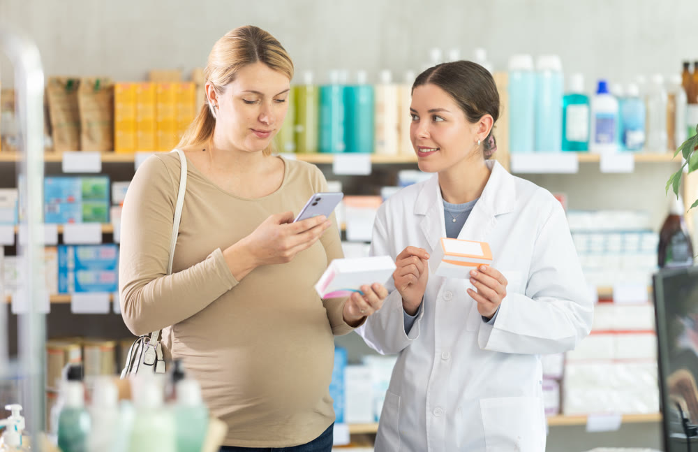 Pregnant woman in pharmacy scans QR code on vitamin pills product, pharmacist consulting client