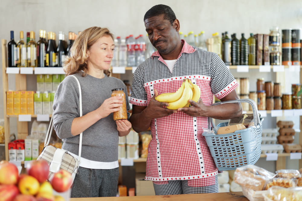 Married couple with various products in hands continuing shopping in grocery department of supermarket
