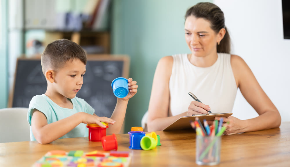 Child psychologist observing boy arranging stacking cups