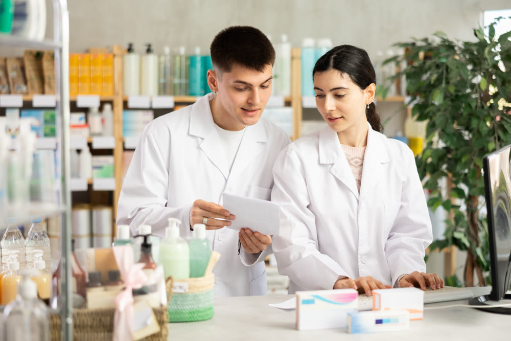 Two male and female pharmacists attentively stocktaking medicines with computer at pharmacy shop