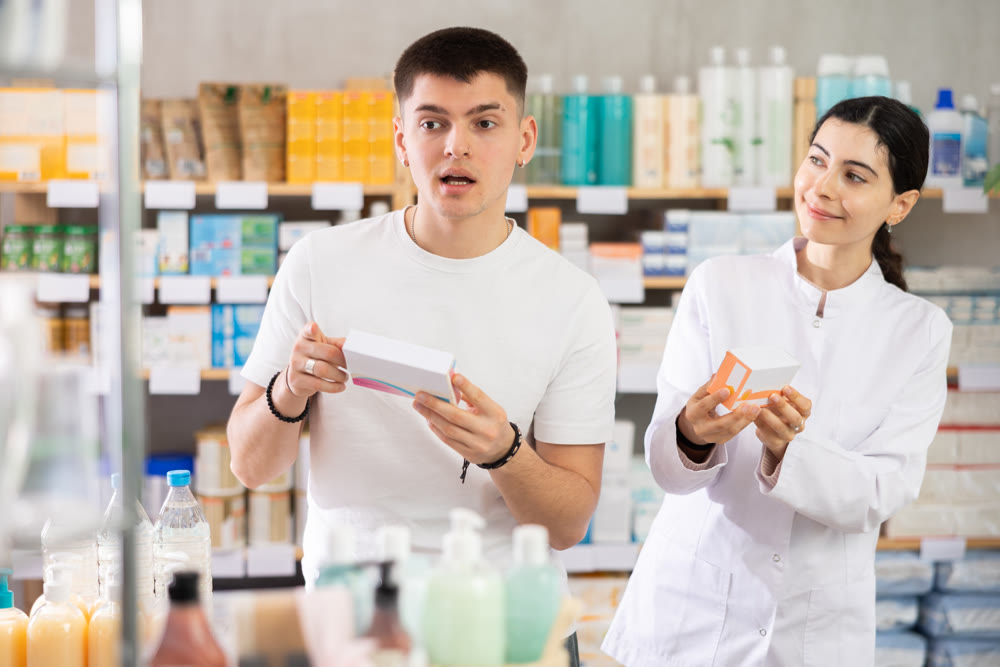 Young man buys pills at drug store, pharmacist in background