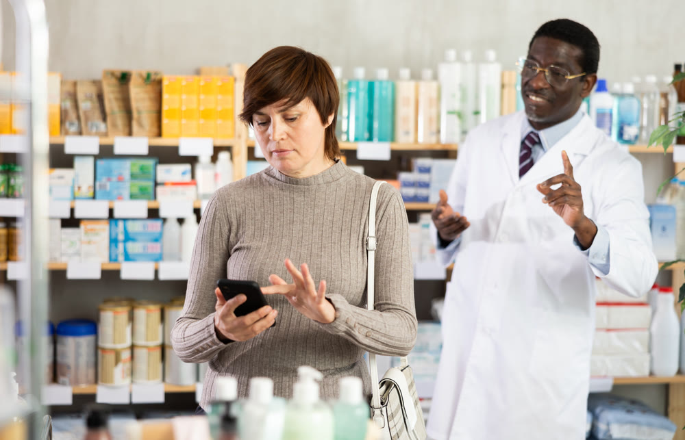 Woman with phone chooses medicines with help of pharmacist