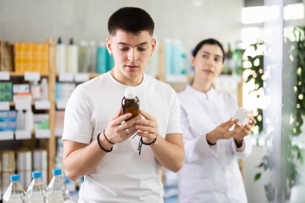Young man buyer selects expectorant syrup, pharmacist offer similar item