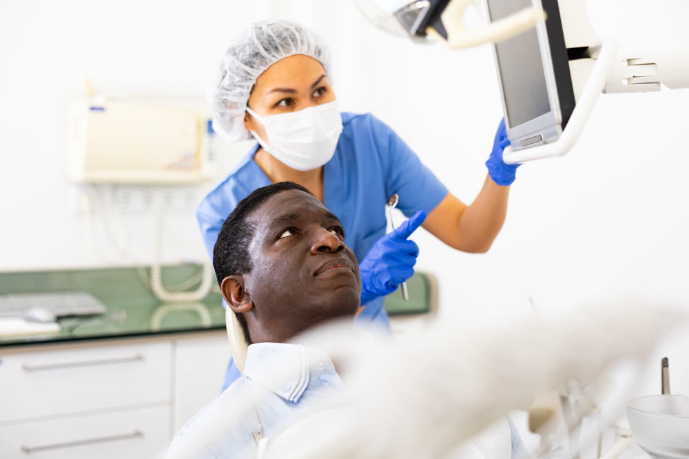 Female stomatologist showing teeth radiography result on computer to patient