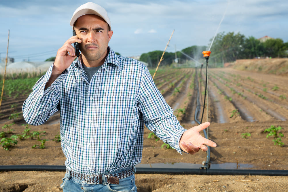 Owner of farm is talking on mobile phone against background of automatic watering machines
