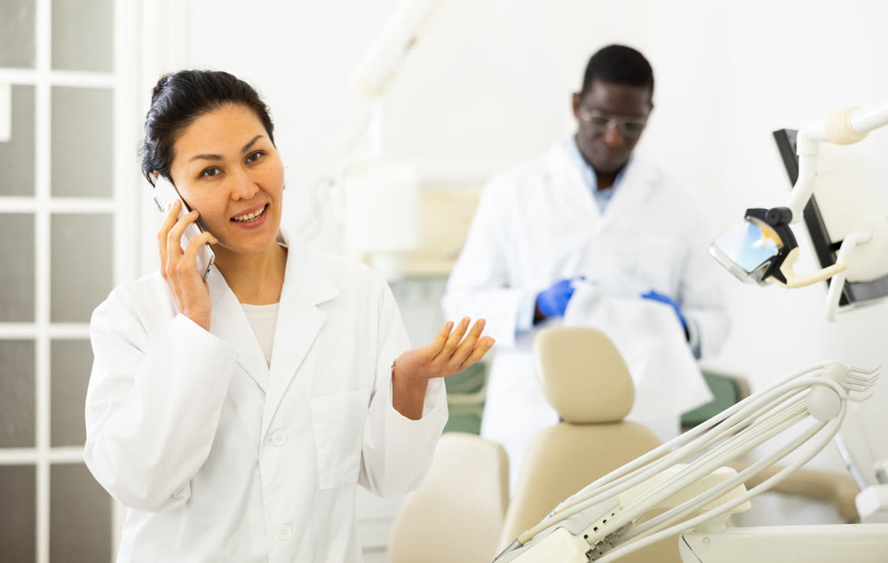 Smiling female dentist talking on mobile phone in dental office