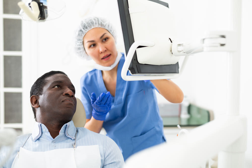 Man sitting on dental chair, female dentist pointing at display