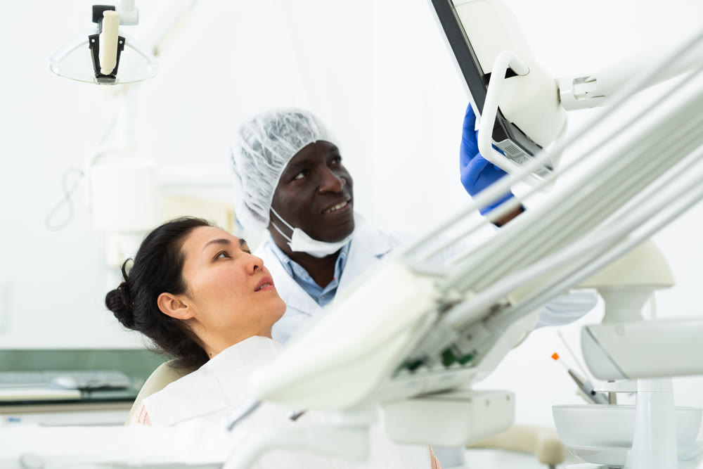 Woman sitting on dental chair, male dentist pointing at display