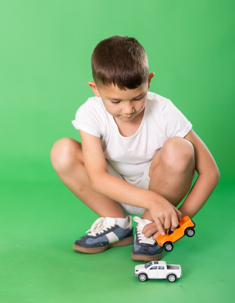 Boy in white clothes playing with toy cars on a green background