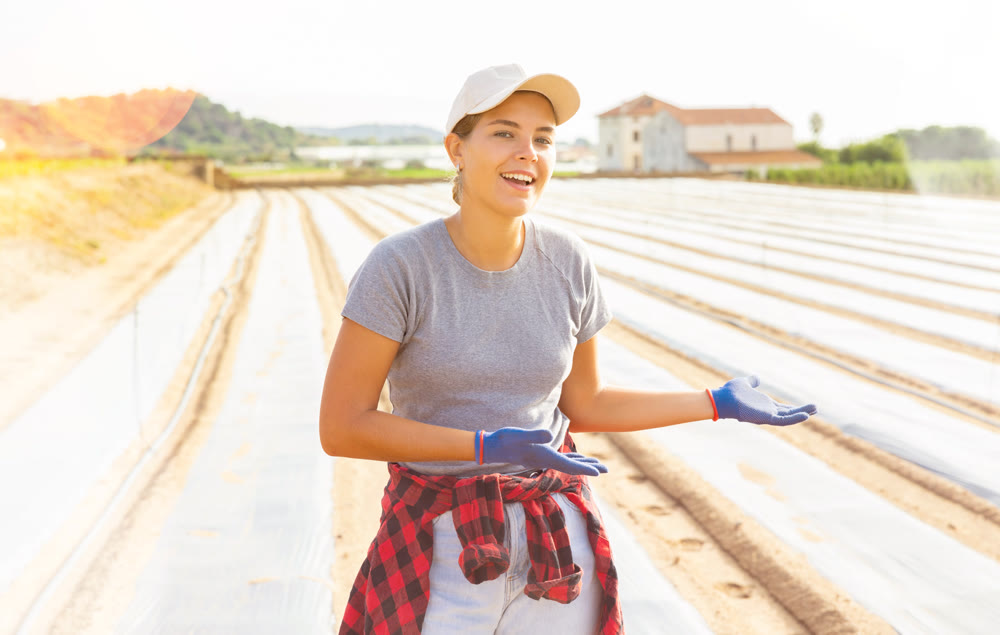 Smiling girl farm worker standing on plantation covered with polyethylene mulch