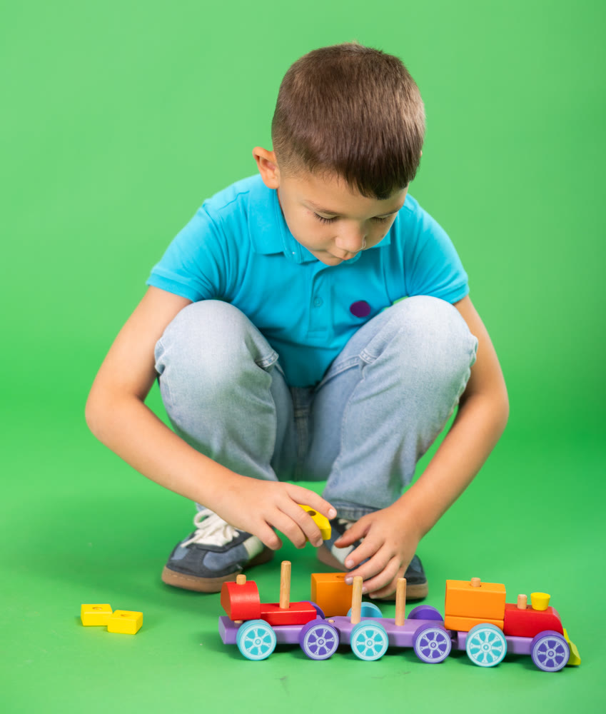 Boy in blue clothes playing with toy wooden train on green background