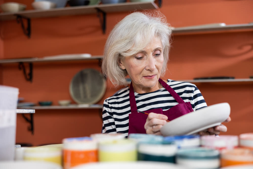 Mature woman ceramist painting new crafted plate