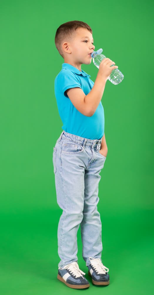 Boy in blue clothes drinks water from a plastic bottle on green background