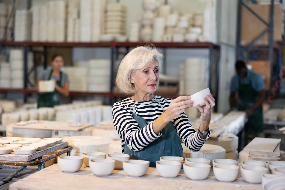 Mature craftswoman checking quality of pottery in pottery factory