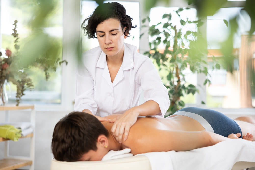 Adult woman giving back massage to young guy