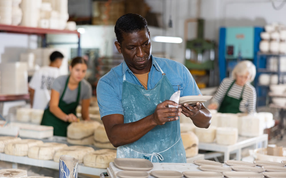 Portrait of african american worker cutting burrs off freshly made earthenware cups and plates with knife
